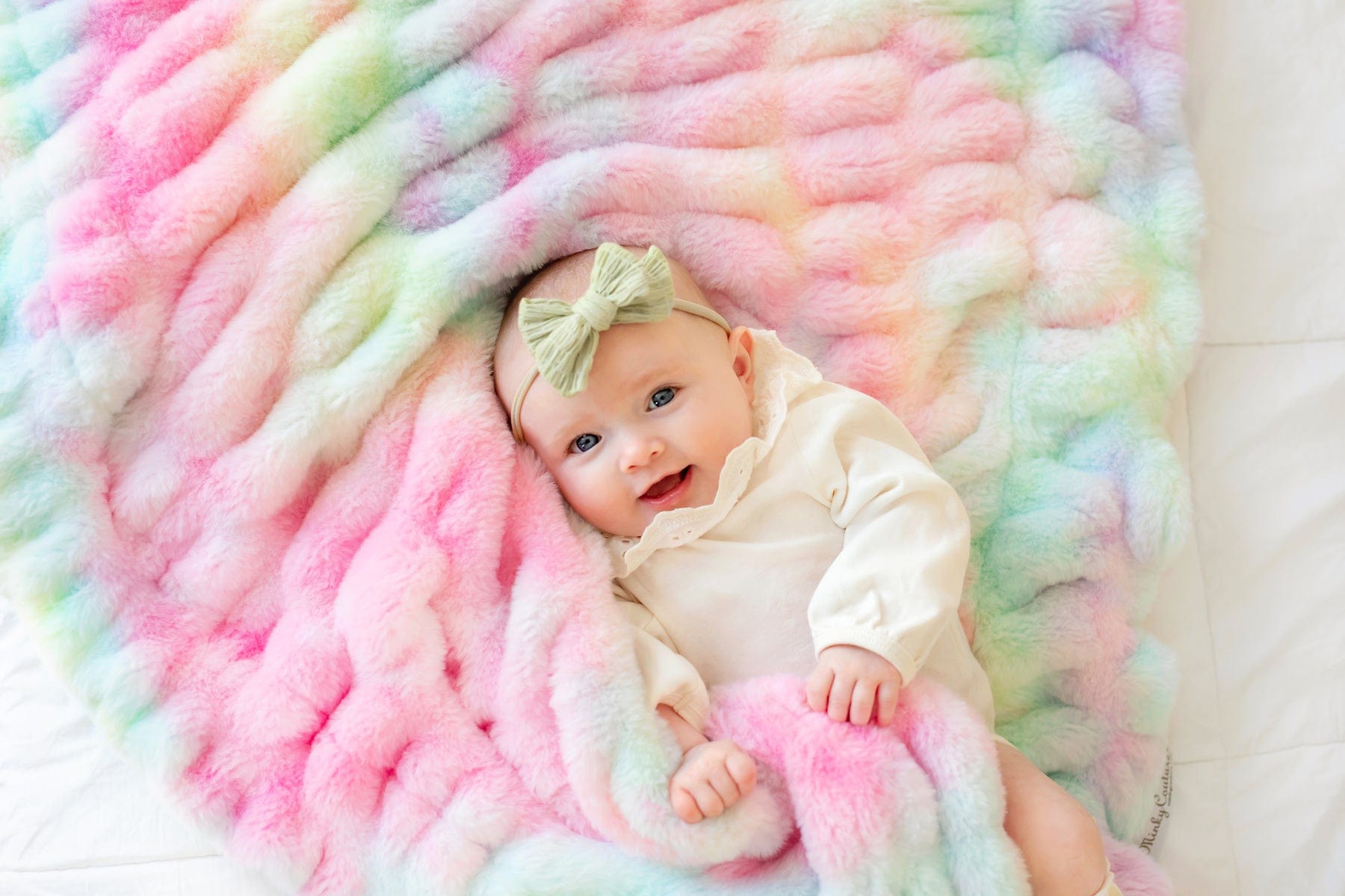 Baby girl laying on a tie dyed pastel stretchy blanket.