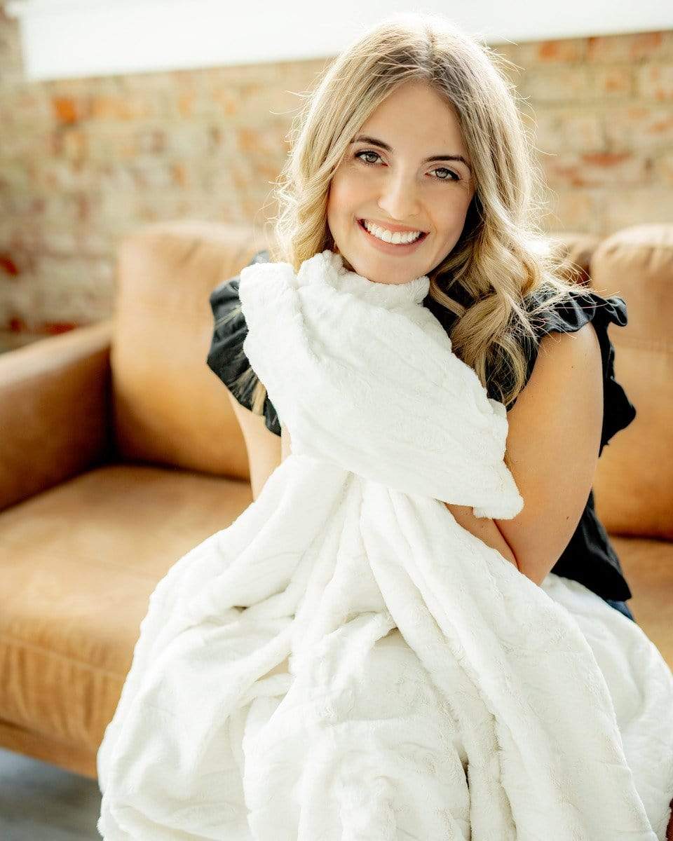 Young woman sitting on a camel colored couch snuggling a thin cream Minky Couture blanket. 